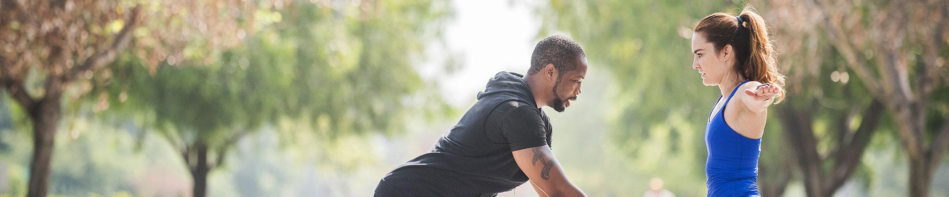 Trainer and client stretching outdoors in a park, getting ready to train