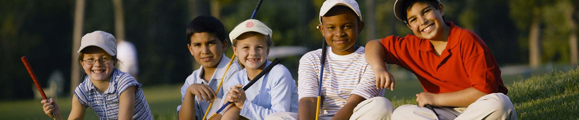 A diverse group of young golfers sitting on the course smiling at the camera