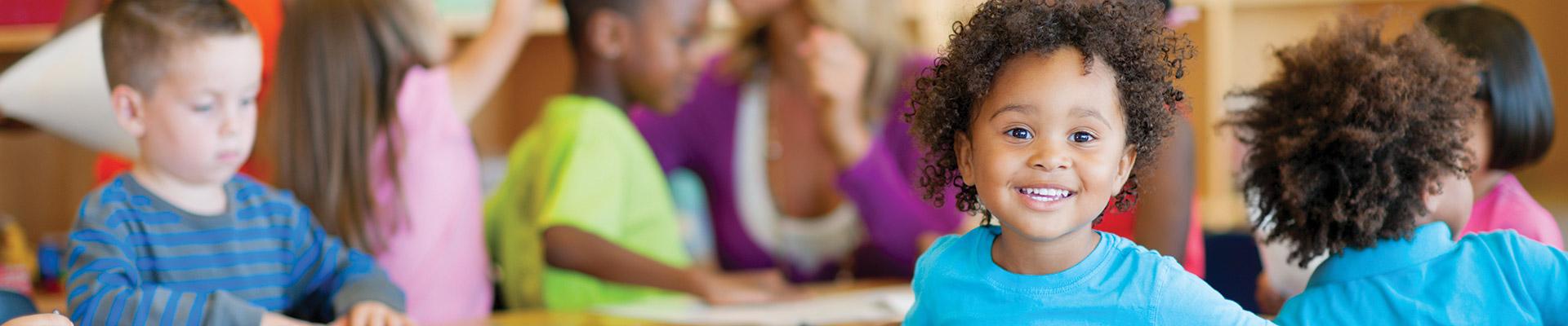 Child sitting at table in preschool smiling at the camera