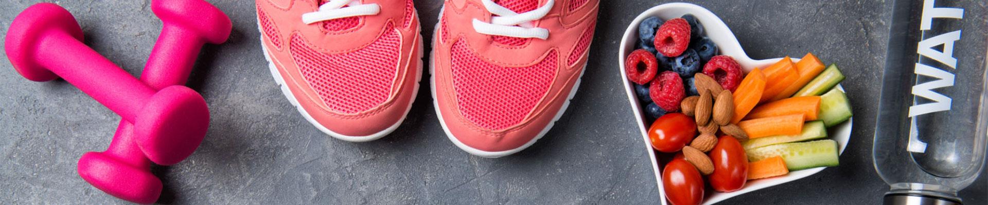 A gray background with small weights, sneakers, healthy snacks and water.