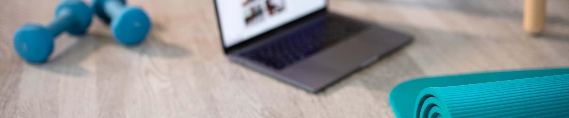Laptop, yoga mat, weights and sneakers on a gray wood floor