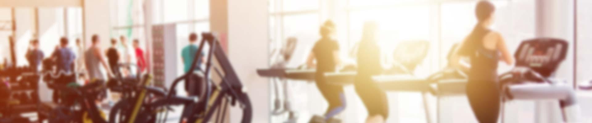 Soft focus image of a busy gym with people working out on weights in the background and people using treadmills in the foreground