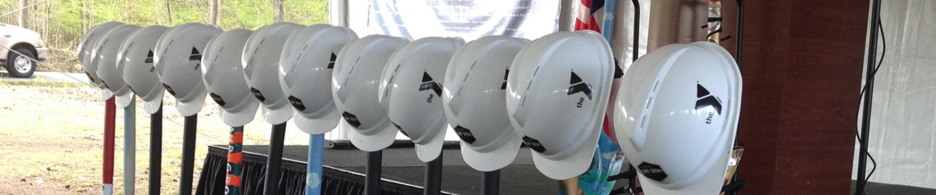 Row of white hard hats with YMCA logo printed, resting on top of shovels at construction site