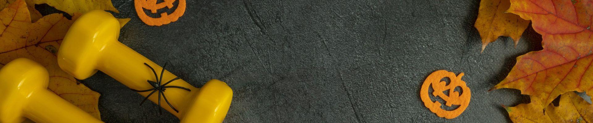 Halloween decorations with gym dumbbells, decorations and autumn pumpkin on fall leaves