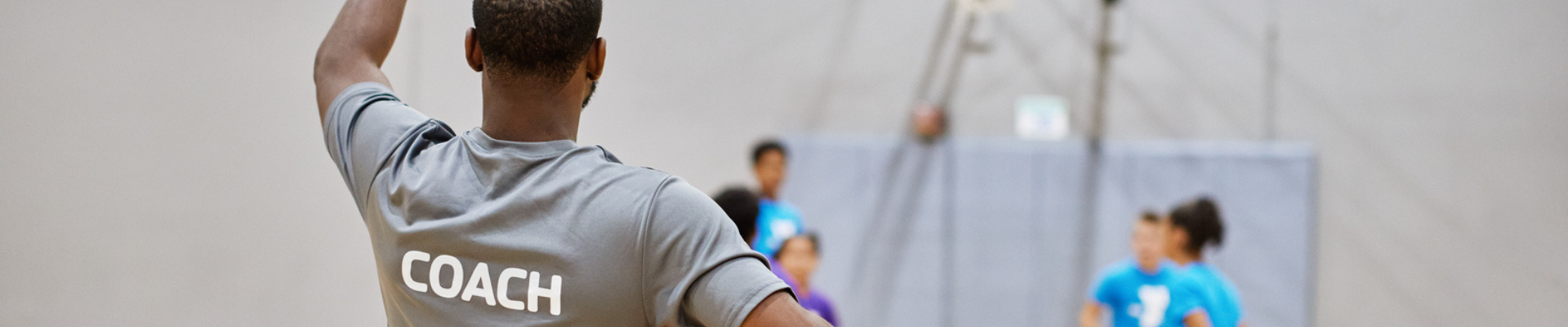 A male YMCA basketball coach teaches five teenagers how to properly shoot basketball at the indoor Y basketball court.