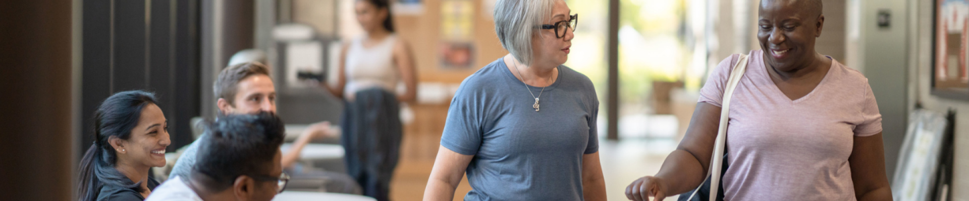 Two women walking down a hallway at the gym with people in the background