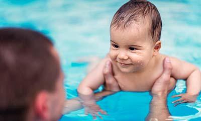 A baby smiles at his dad while his dad holds him afloat in the pool