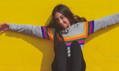 Teen sits with her arms out in front of a yellow wall