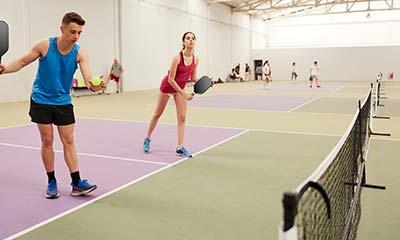 Two pickleball players stand on the court, one in ready position while the other prepares to serve.