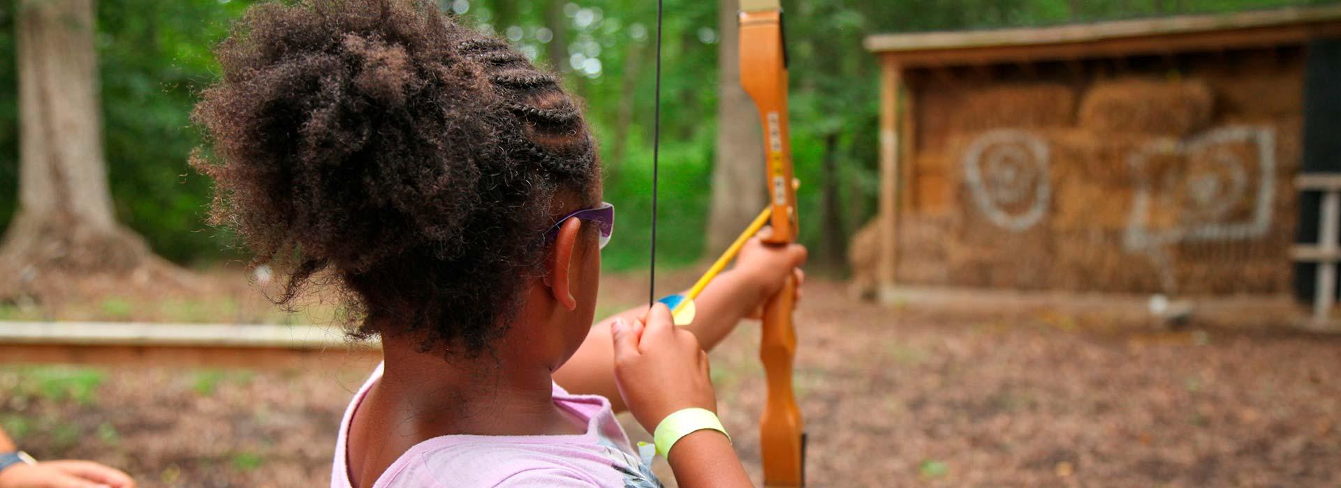 Young girl aiming with bow and arrow at a hay target at YMCA Camp Arrowhead in Suffolk, Virginia