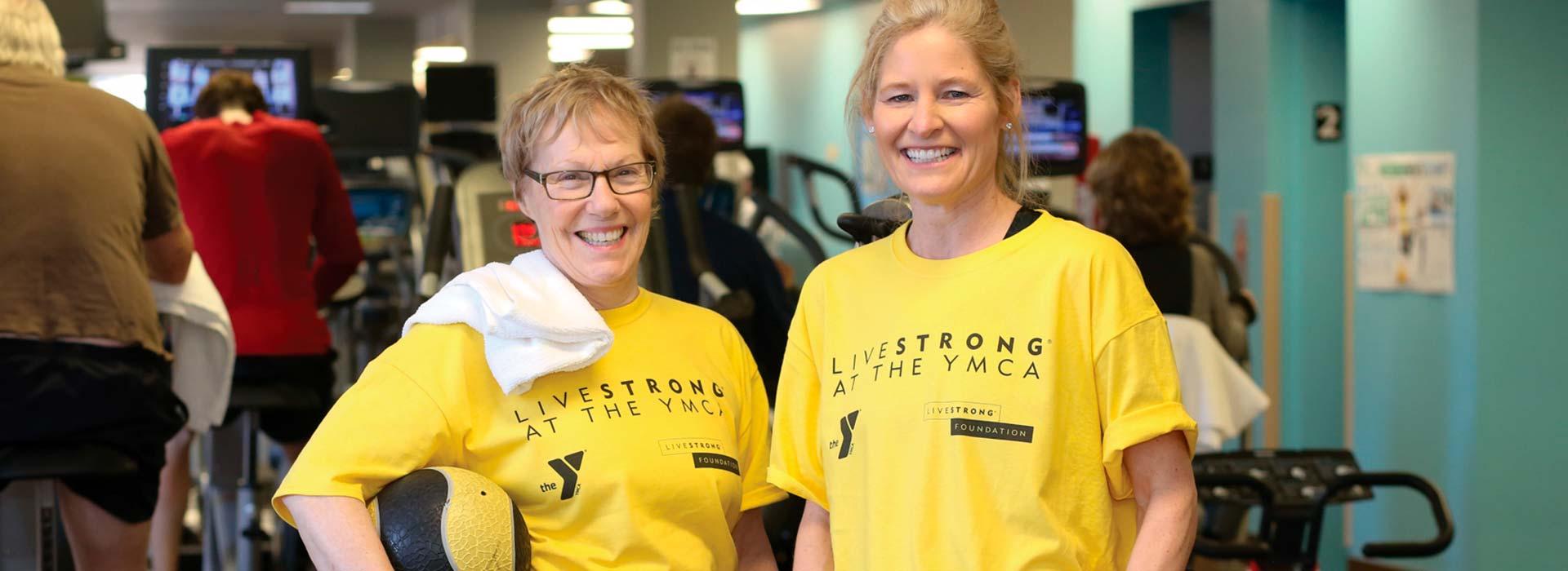 Two LIVESTRONG at the YMCA participants smiling at the camera with the Wellness Center in the background