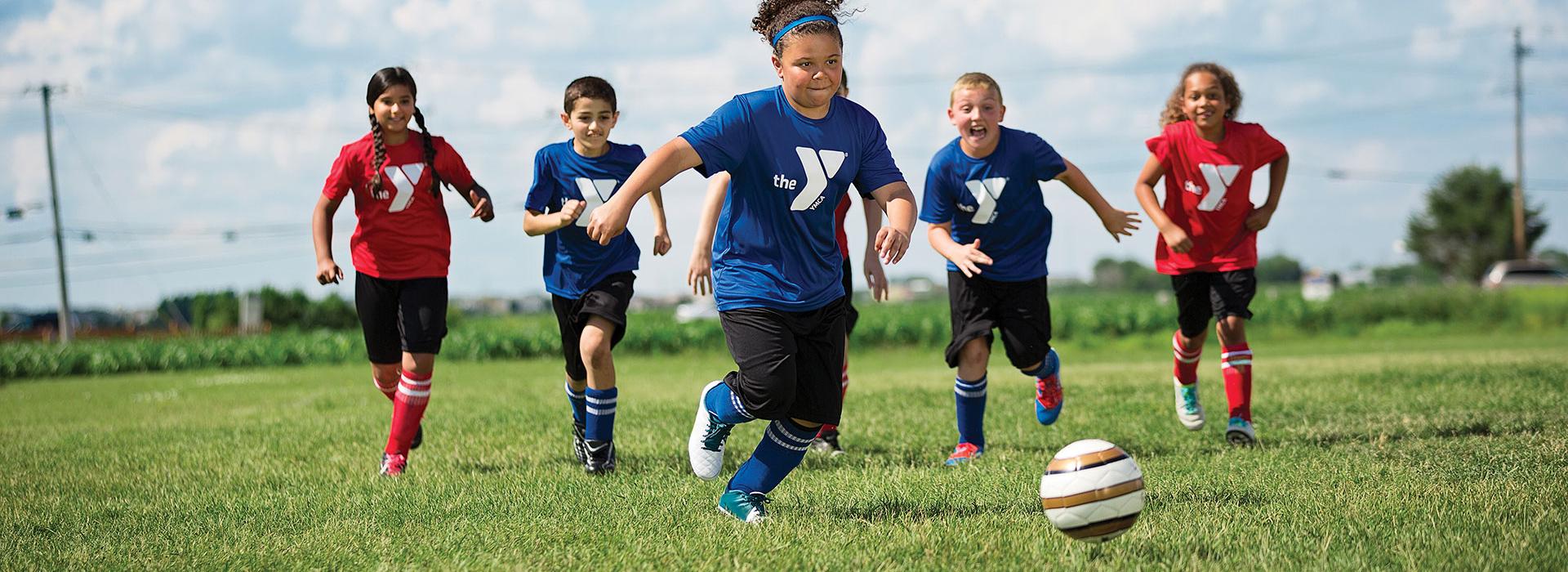 Diverse group of children in YMCA shirts playing soccer outdoors