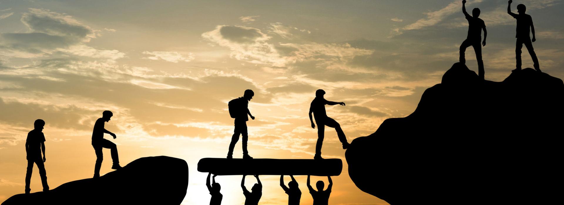 A group of people holding up a rock so that others can use it as a bridge