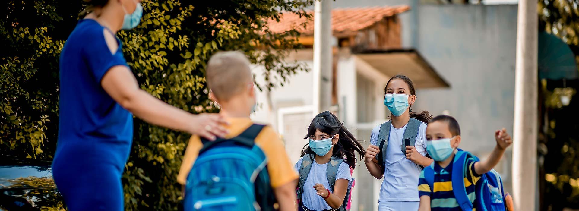 Mom dropping her child off at care, where three masked children are excited to see their friend.