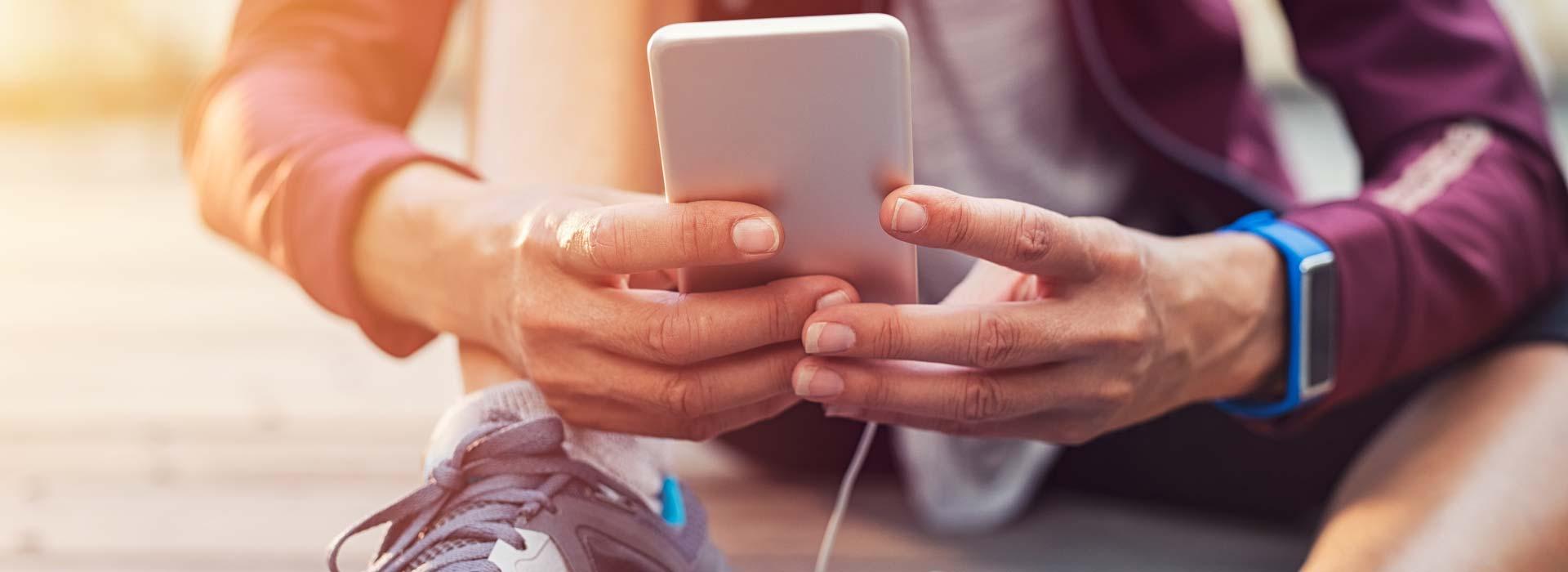 A person wearing fitness attire sitting on the ground and holding phone