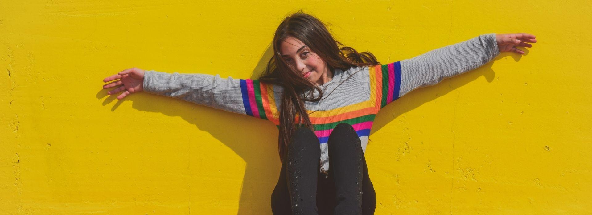 Teen sits with her arms out in front of a yellow wall