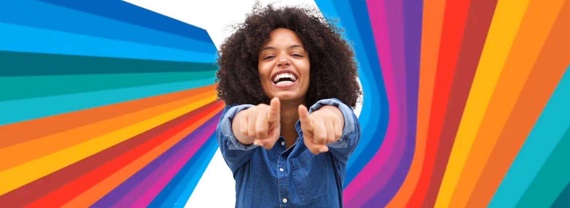 Dynamic multicolor backdrop with a smiling woman looking at you, with both fingers pointing toward you.