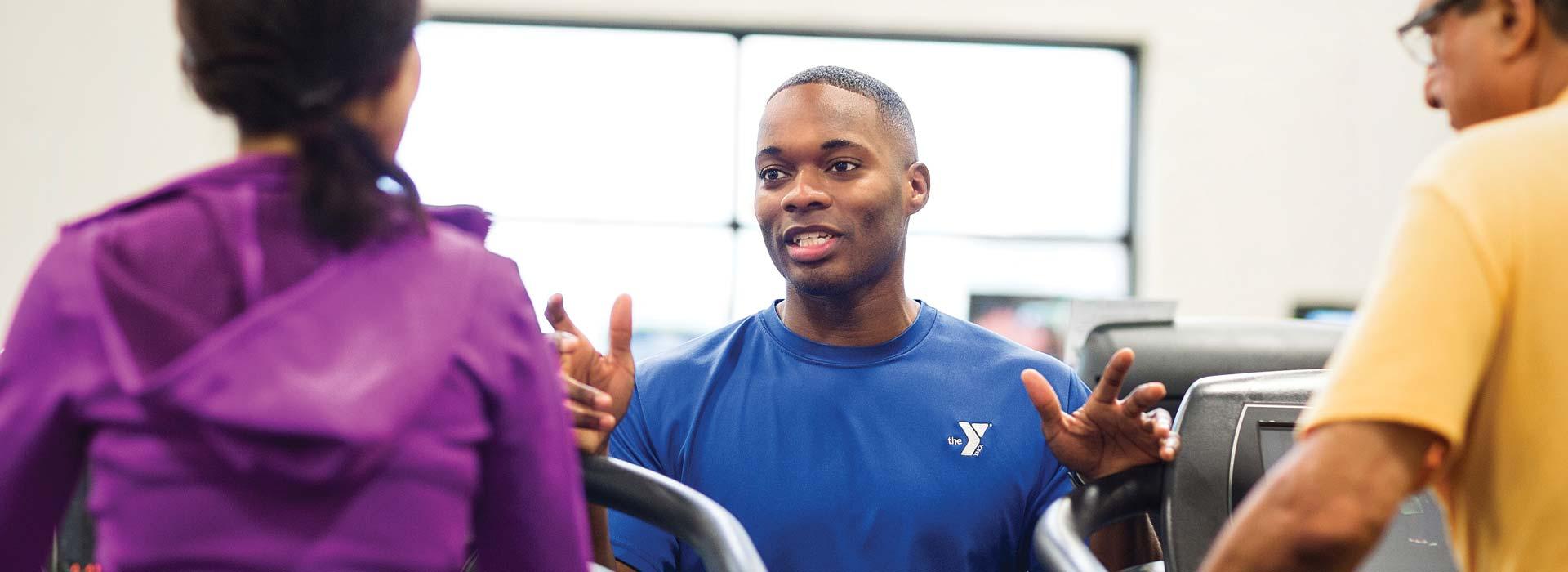 YMCA fitness staff person talks to two members using cardiovascular equipment in the Y's wellness center.