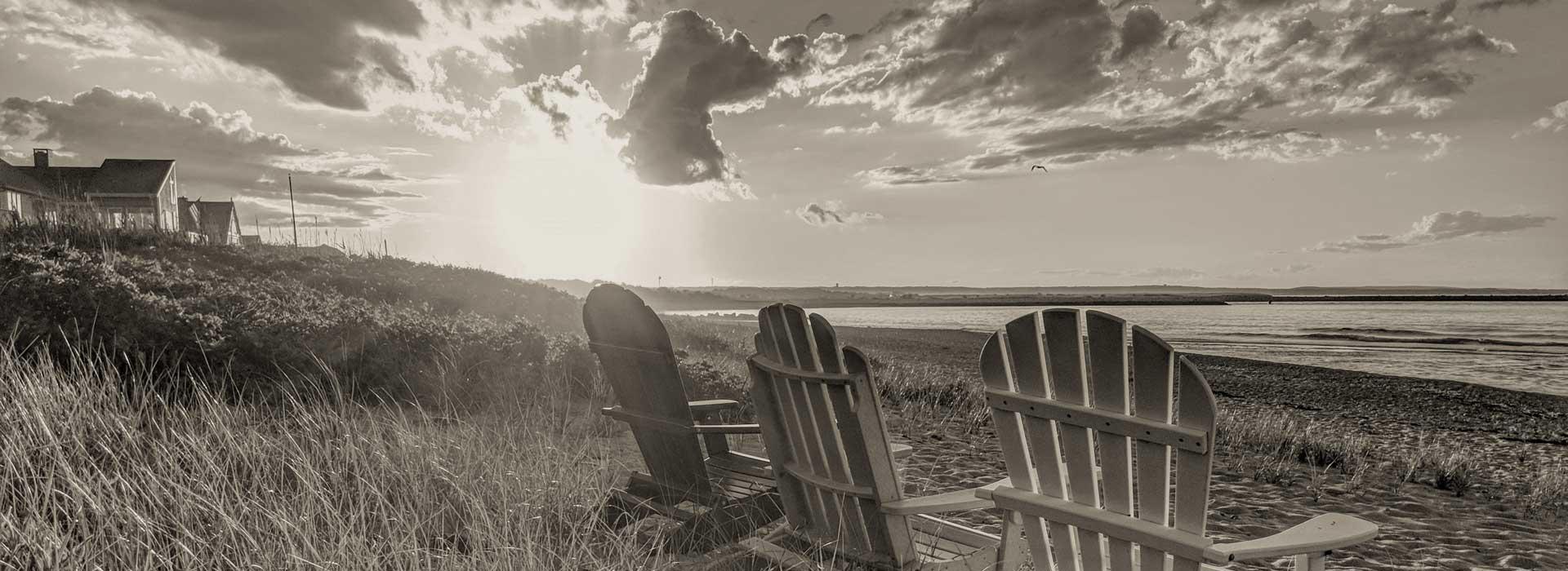 Adirondack chairs on the beach with beach houses in the background